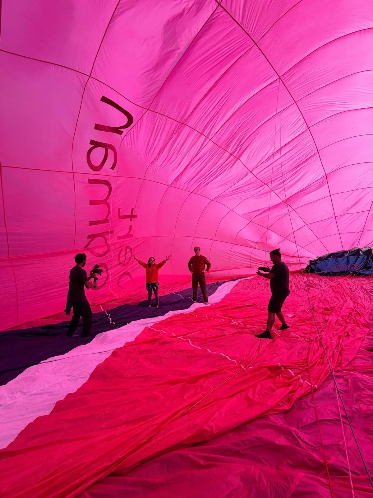 Inside a partly inflated hot air balloon: panels of pink, red and white fabric curving overhead towards the crown.