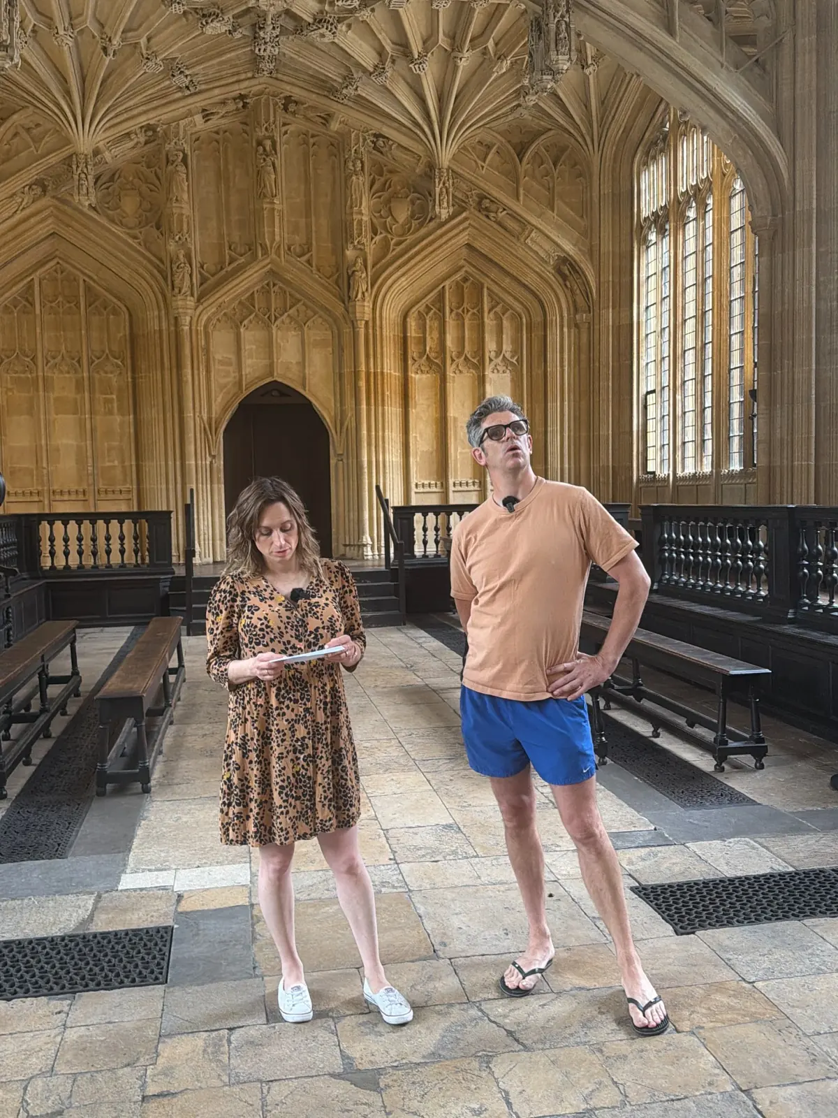 Two presenters looking up at the fan-vaulted ceiling of the Divinity School at Oxford's Bodleian Library.