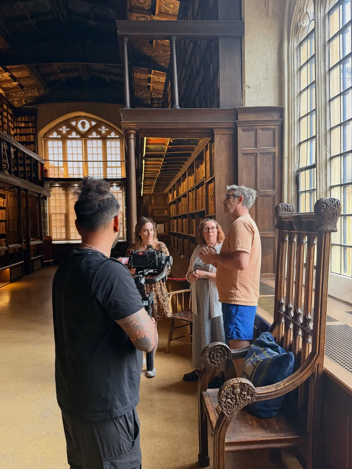 A camera operator on a gimbal filming an interview between the galleried bookshelves of an Oxford library.