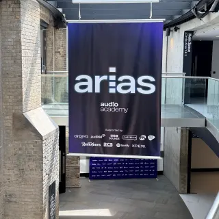 An ARIAS banner listing the sponsors hanging above the stairs in the Roundhouse foyer, between old brick walls and a glass balcony.