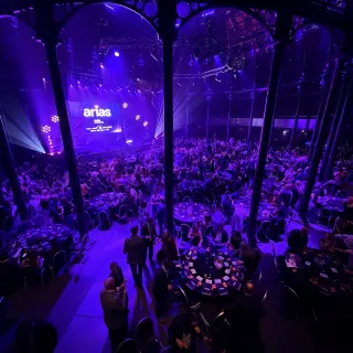 Looking down on the packed Roundhouse from the balcony during the ARIAS, guests at round tables scattered with cards, the stage glowing purple at the far end.