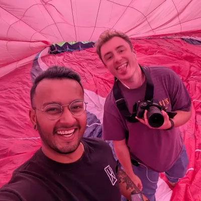 Two crew grinning for a selfie inside the pink balloon envelope, one holding a Sony camera, everything lit rose by the fabric.