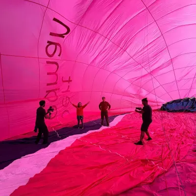 Inside a partly inflated hot air balloon: panels of pink, red and white fabric curving overhead towards the crown.