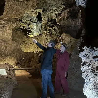 Underground at Clearwell Caves: a freeminer in a maroon boilersuit and head torch points up at the rock ceiling while a second man looks where he is pointing.