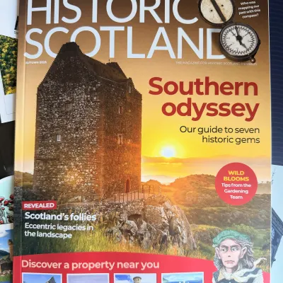 The Autumn 2026 issue of Historic Scotland, cover line 'Southern odyssey', a tower house lit by a low sun, resting on a pile of Loganair boarding passes and postcards.
