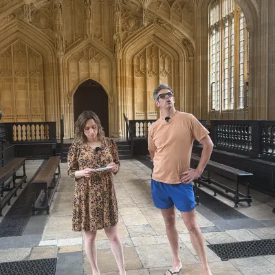 Two presenters looking up at the fan-vaulted ceiling of the Divinity School at Oxford's Bodleian Library.