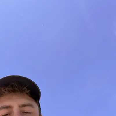 A selfie taken from below against a cloudless deep blue sky, only the top of a face and a cap in the bottom corner.