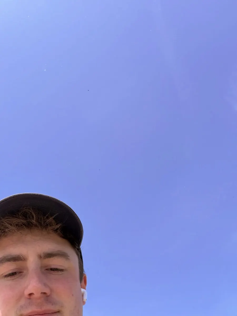 A selfie taken from below against a cloudless deep blue sky, only the top of a face and a cap in the bottom corner.